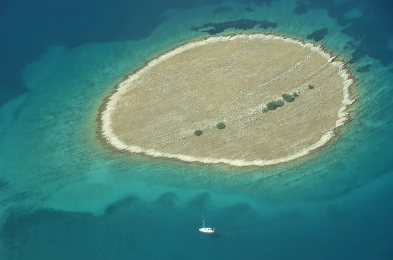A small islet in turquoise water with a boat at anchor beside it