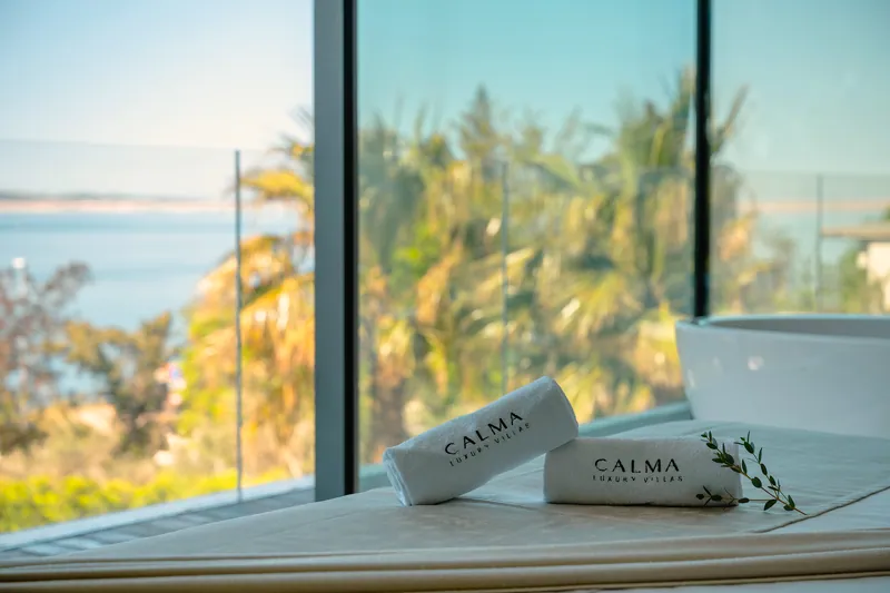 Calma towels by the bath, with palms and the sea through the glass