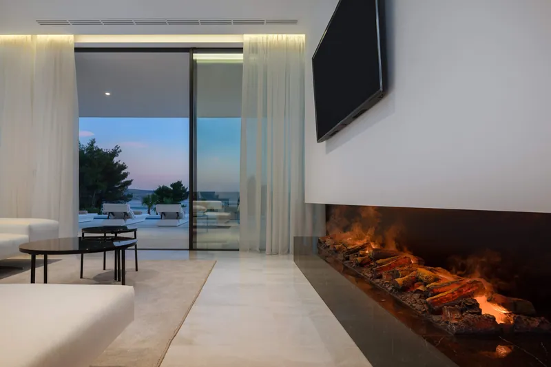 The living room and its fireplace at dusk, with the terrace beyond